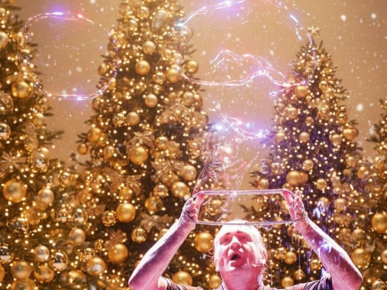 Mann mit Glitzer und Seifenblasen vor festlich geschmückten Weihnachtsbäumen.