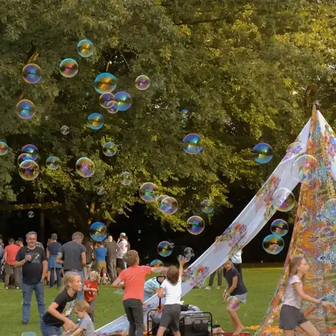 Kinder spielen mit Seifenblasen vor einem bunten Zelt im Freien.