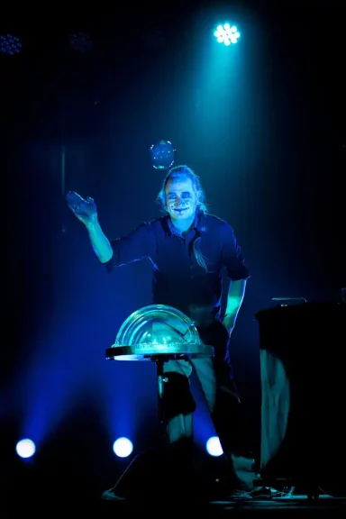 Fliegende Seifenblase in der Seifenblasenshow von Stephan Masur Ein Performender in blauer Beleuchtung mit einer großen, runden Requisit.