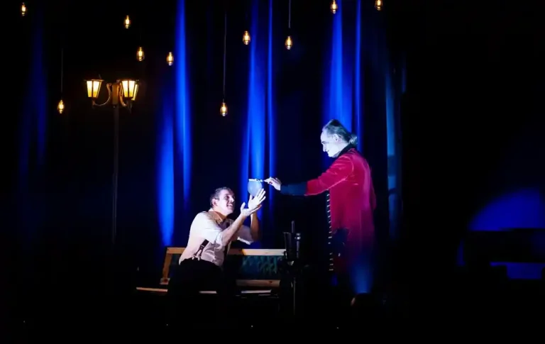 interaktive Seifenblasenshow Zwei Schauspieler auf der Bühne, einer kniet und reicht dem anderen etwas. Beleuchtung in Blau.