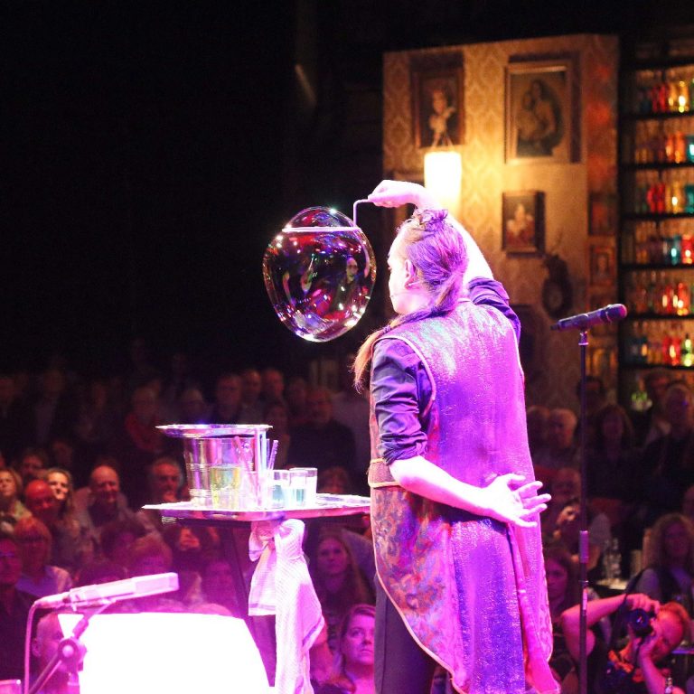 Eine Künstlerin bläst Seifenblasen auf einer Bühne vor einem begeisterten Publikum.