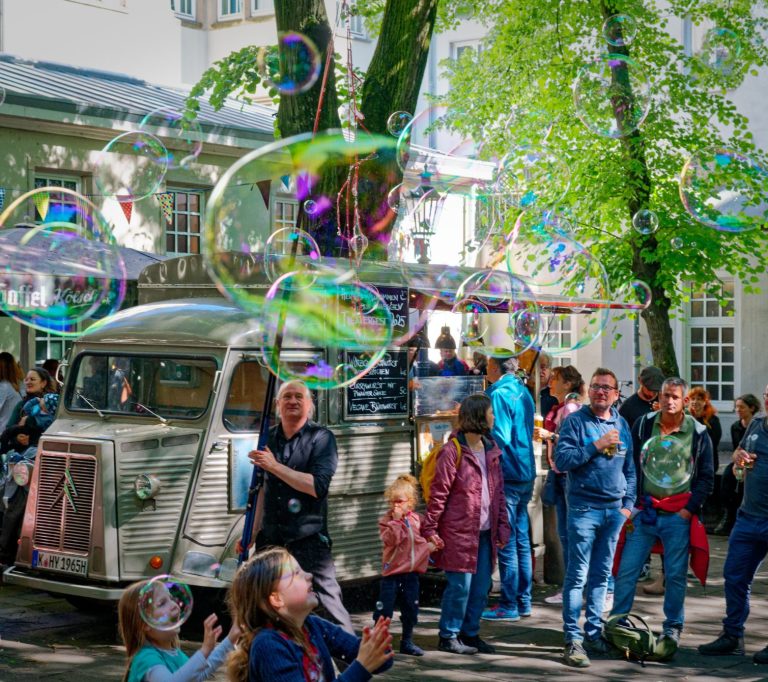 Hochzeit Seifenblasen Eine Gruppe von Menschen steht um einen alten Truck, umgeben von großen Seifenblasen.