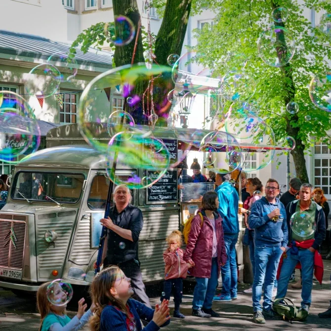 Menschen stehen vor einem Foodtruck, umgeben von großen, schillernden Seifenblasen.