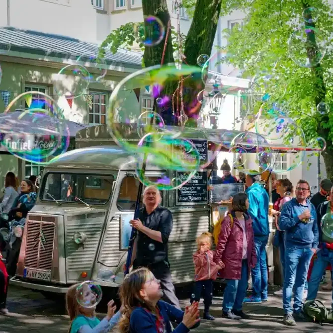 Seifenblasen Walk Act Masur Wiesbaden Menschen stehen in einem Park, während große Seifenblasen durch die Luft schweben.