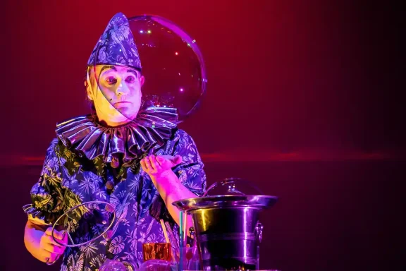 poetische Seifenblasenshow mit Riesenseifenblase Ein clownartiger Darsteller mit buntem Kostüm und großen Seifenblasen auf einer Bühne.