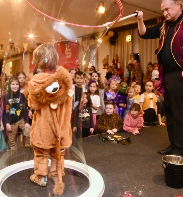 Kind in Bubble sensorische Seifenblasenerlebnis Ein Kinderzauberer zeigt eine Seifenblasen-Demonstration vor vielen jubelnden Kindern.