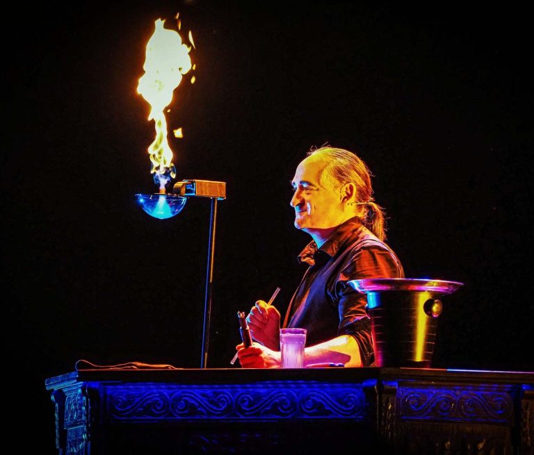 Brennende Seifenblase Magier mit einem Feuer effet während einer Vorstellung, lächelt und hält ein Glas.