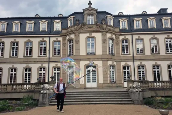 Riesenseifenblase Walkact Büsing Palais Person mit einem bunten Regenschirm vor einem historischen Gebäude.