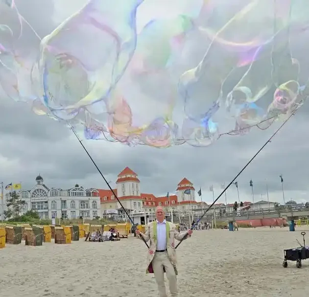 Seifenblasensturm mit Riesenseifenblasen am Strand Ein Künstler macht riesiege Seifenblasen mit Angeln am Strand vor einem Kurhaus