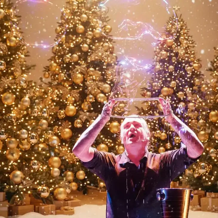 Stephan Masurs wunderbare Seifenblasenshow für Weihnachten Ein Seifenblaenkü+sntler pustet grosse Seifenblasen durche ine große Schjlaufe vor goldenen Tannenbäumen