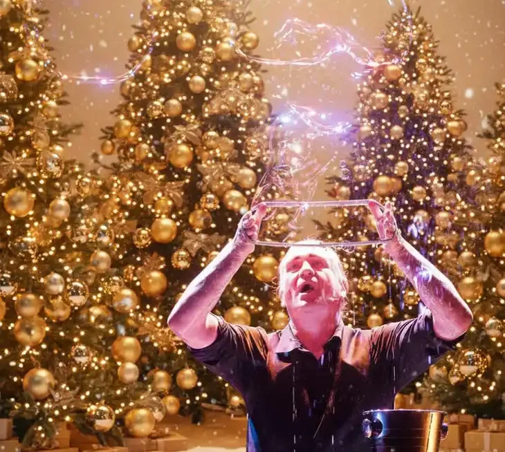 Stephan Masur Seifenblasen Weihnachtsfeier Ein Mann blässt Seifenblasen mit einer Schlaufe vor Weihnachtsbäumen