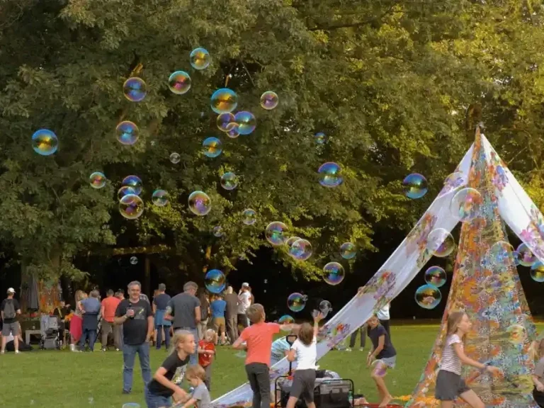 Seifenblasen Wellness Event Bunte Seifenblasen schweben über eine belebte Parkszene mit einem Zeltdorf.
