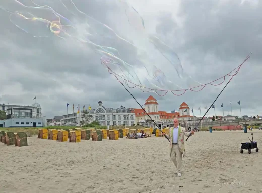 Seifenblasensturm am Strand Person am Strand hält bunte Schnüre in der Hand, im Hintergrund Strandkörbe und Wolken.