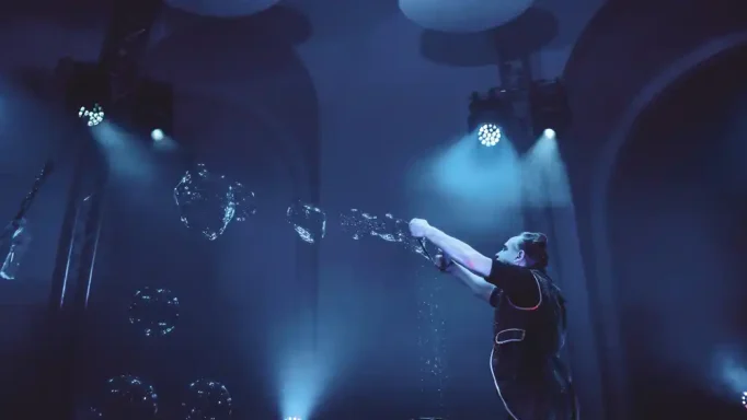 Seifenblasensturm von Stephan Masurs Wunderbarer Seifenblasenshow Eine Person in einem dunklen Raum erzeugt Blasen mit einem speziellen Gerät unter blauen Lichtern.