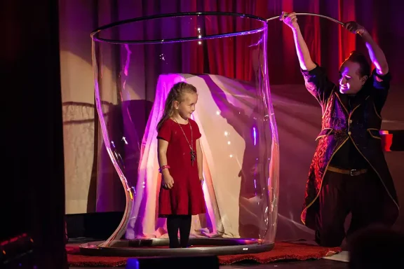 Ein Mädchen in einem roten Kleid steht in einer transparenten Blase auf der Bühne.
