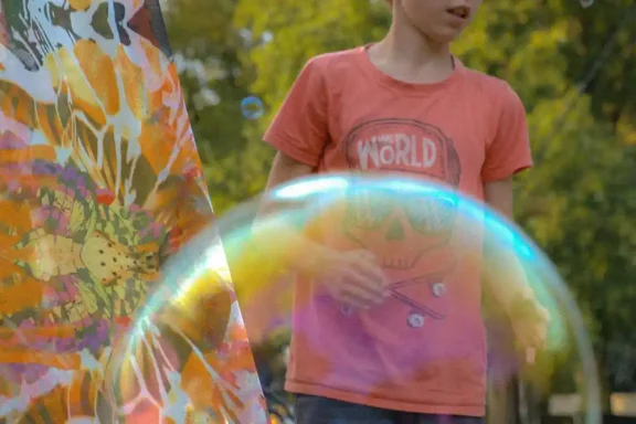 Schimmernde Seifenblase Ein Junge mit T-Shirt steht neben einer farbenfrohen Seifenblase im Freien.