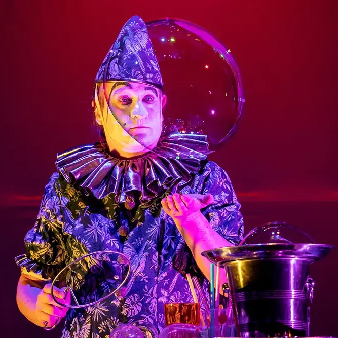 Stephan Masurs Seifenblasenshow als Clown Eine verkleidete Person mit buntem Kostüm und einer Seifenblase in der Hand.