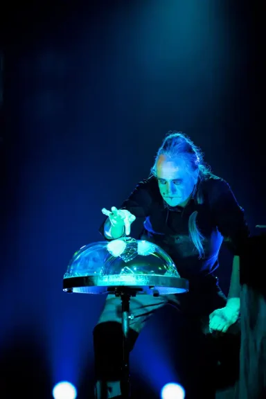 Komplexe Seifenblasenskulptur in Seifenblasenshow Ein Musiker spielt mit einer Glaskugel unter blauem Licht.