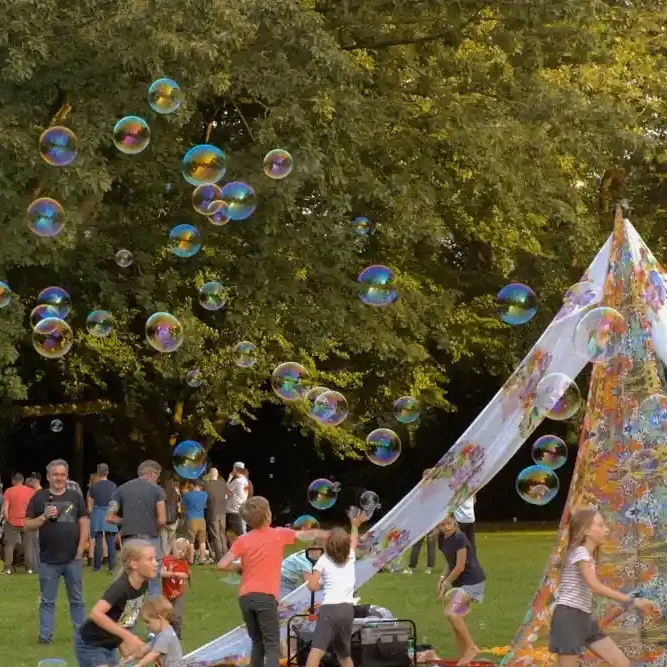 interaktiver Seifenblasenworkshop Menschen spielen im Freien, umgeben von Seifenblasen und einem bunten Zelt.