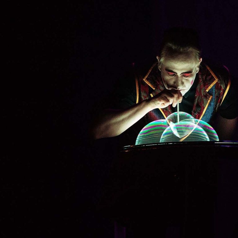 Seifenblasenshow Domes Stephan Masur Ein Künstler bläst Seifenblasen während einer Performance in dunkler Umgebung.