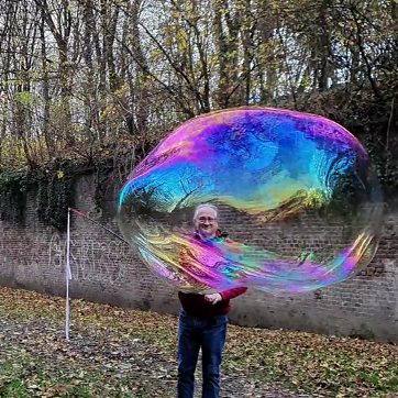 Riesenseifenblase Stephan Masur Mann hält eine große, bunte Seifenblase vor einer herbstlichen Landschaft.