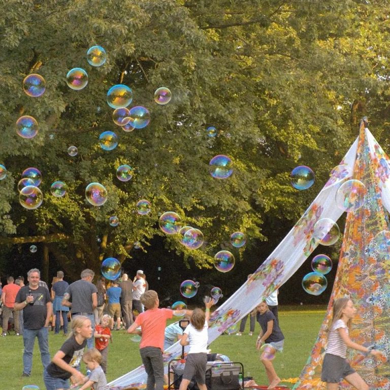 Kinder spielen mit Seifenblasen vor einem bunten Zelt im Freien.
