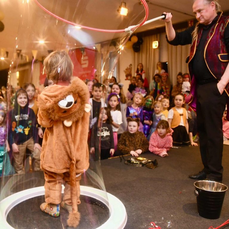 Ein Kind in einem Löwenkostüm steht in einer Seifenblase, während ein Magier zusieht.
