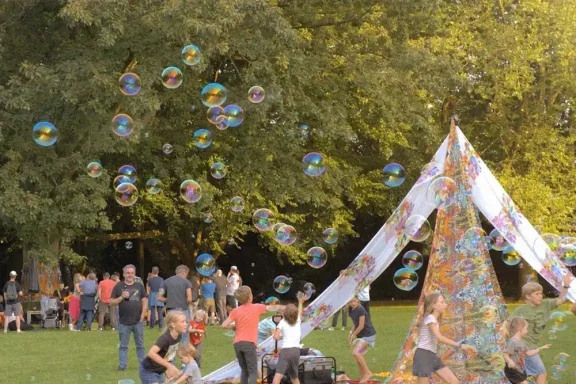 Seifenblasensturm vor Zelt Bunte Seifenblasen schweben über einer bunten Zeltformation und einer fröhlichen Menschenmenge.