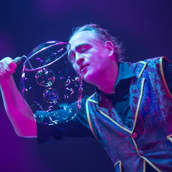Stephan Masur mit Wunderbare Seifenblasen bei einer Seifenblasenshow für Varieté und Theater auf der Bühne Zauberer formt mit einer großen Seifenblase, violette Beleuchtung im Hintergrund.