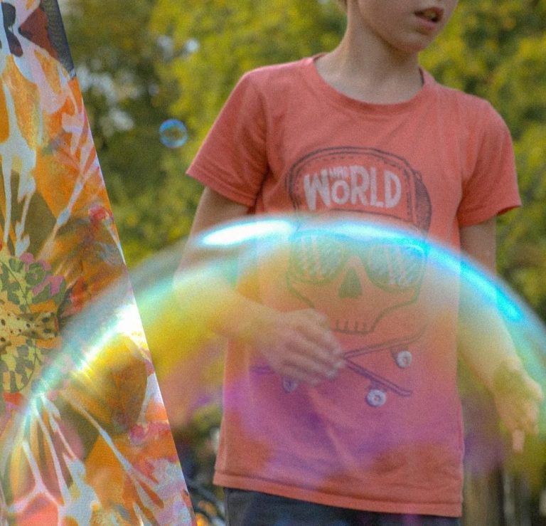 Junge in Shirt mit Totenkopf-Design, während er Seifenblasen beobachtet.