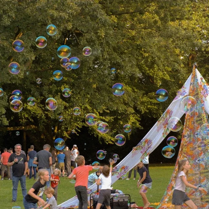 Kinder spielen im Freien, umgeben von Seifenblasen und einem bunten Zelt.