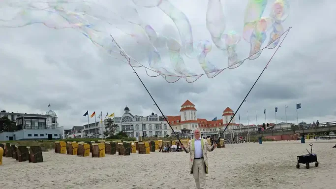 Seifenblasen fun am Strand Mann am Strand, der riesige Seifenblasen mit langen Schnüren kreiert.