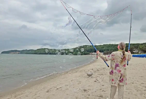 Seifenblasen Beach Frau am Strand mit Netz, fängt Fische im flachen Wasser bei bewölktem Himmel.