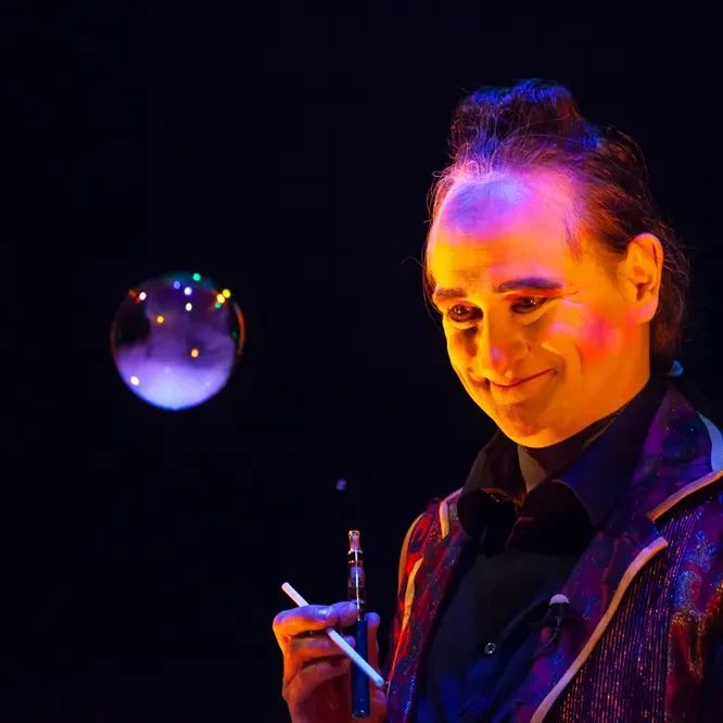 Charakter auf der Bühne – Narrative Performance mit Seifenblasen Lächelnder Künstler mit Seifenblase, umgeben von buntem Licht.