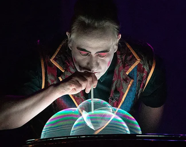 Clown bläst Seifenblasen mit bunten Lichtern im Hintergrund.